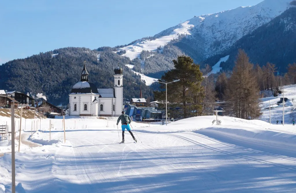 Langrennsløper i solfylt løype mot pitoresk kirke, Seefeld, Østerrike