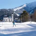 Langrennsløper i solfylt løype mot pitoresk kirke, Seefeld, Østerrike