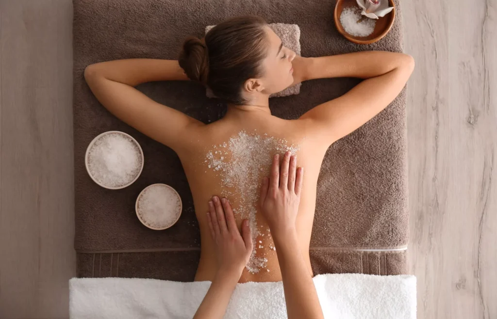 Mujer joven que se somete a un procedimiento de exfoliación corporal con sal marina en un salón de spa, vista superior